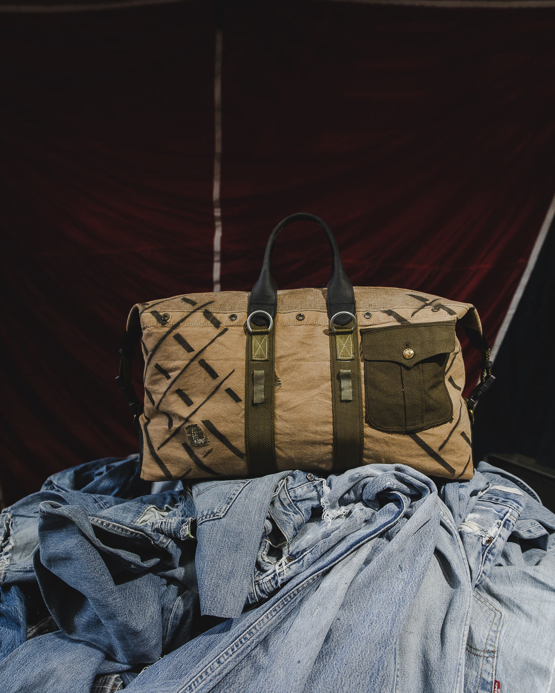 Brown leather bag with black patterns on a pile of blue jeans against a dark background
